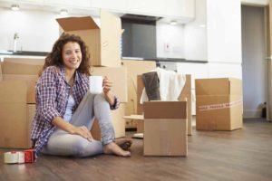 Woman Moving Into New Home And Unpacking Boxes Sitting On Floor